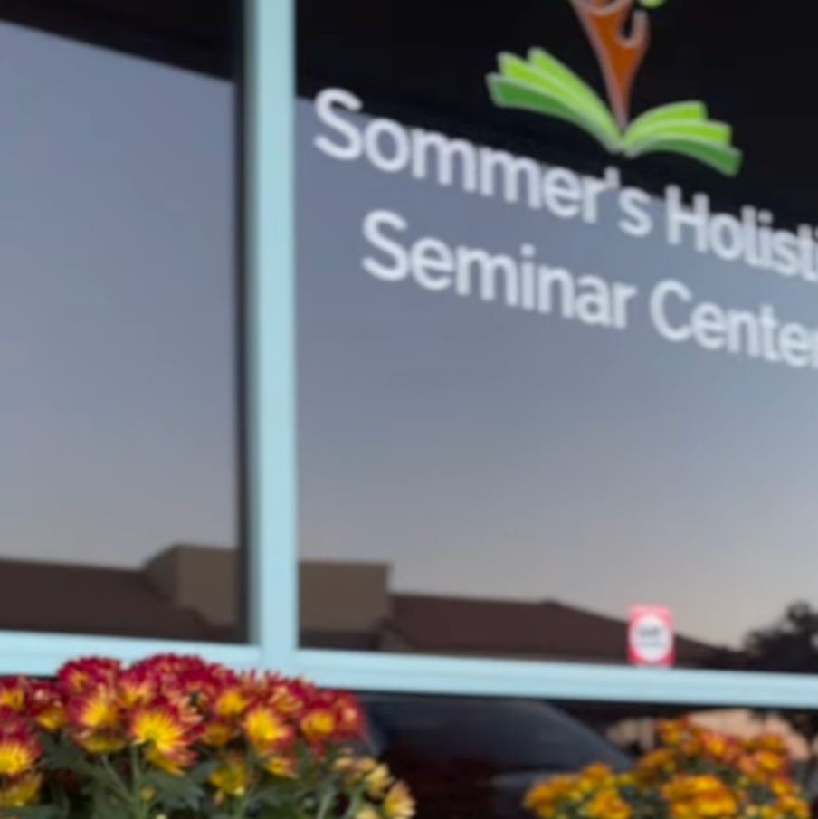 Decorative display with pumpkins and flowers in front of a screen displaying 'Sommer's Holistic Seminar Center'.