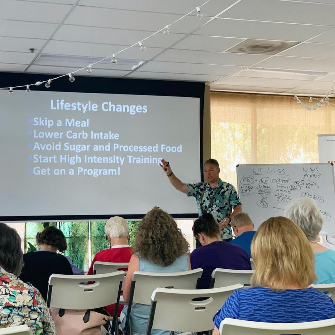 Scott giving a presentation to an audience with a screen displaying lifestyle changes.